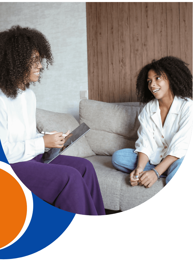 Two women sitting on a couch talking to each other.