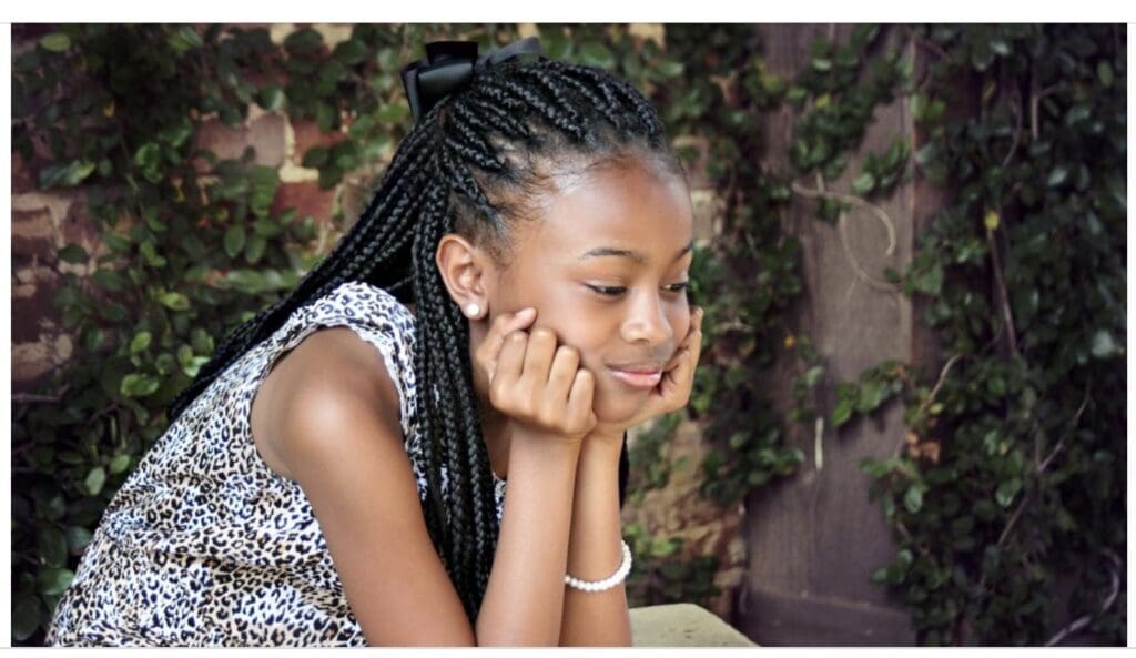 A young girl with braids sitting on the ground.