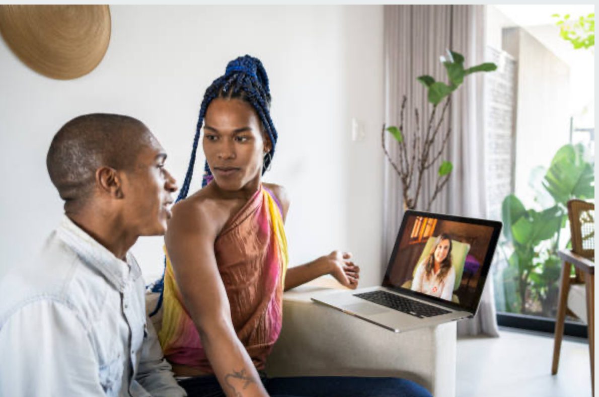 Two people sitting on a couch looking at a laptop.