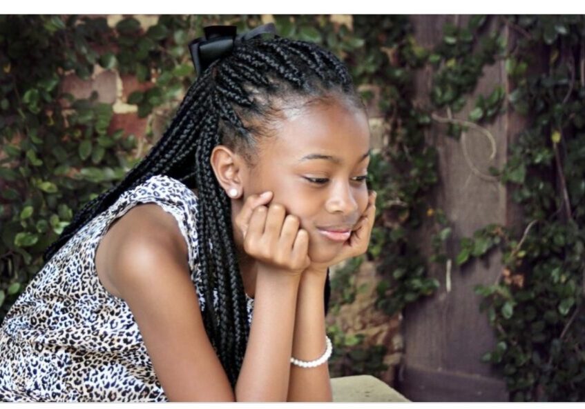 A young girl with braids sitting on the ground.