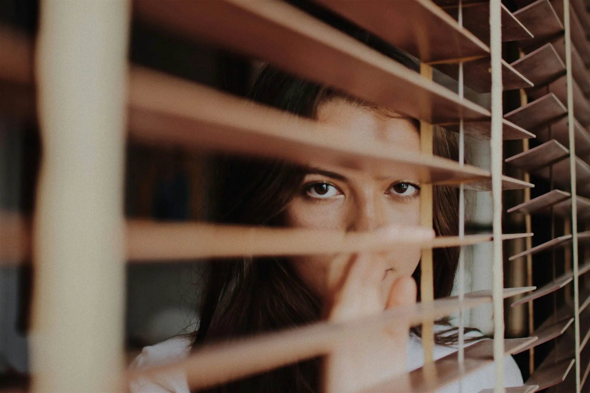 Woman peering through wooden blinds.